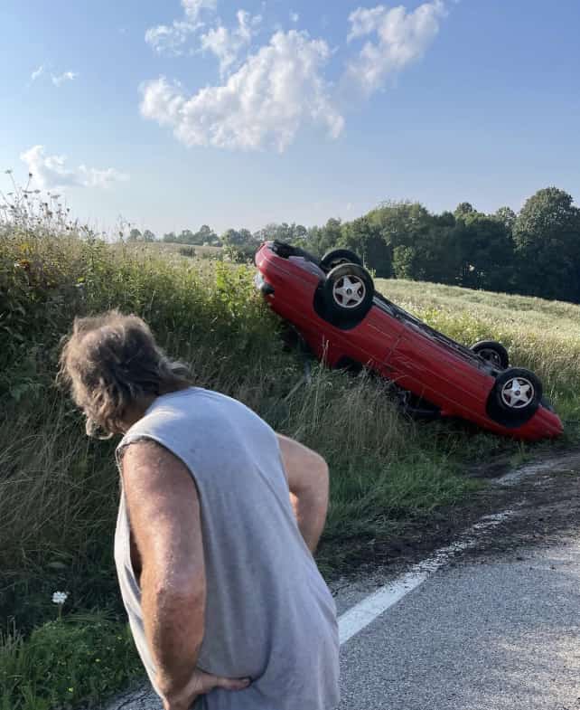 Car overturned on the road on a sunny day with a man holding his hips